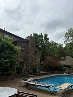 Backyard pool beside a brick house with lounge chairs under a cloudy sky