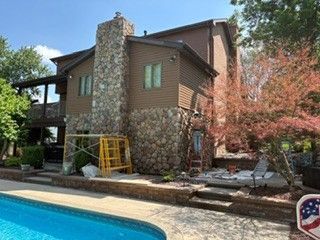 House with stone and wood exterior beside a swimming pool, with trees and outdoor patio furniture