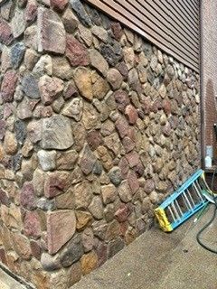 Stone wall beside a sidewalk with a blue ladder leaning against it and a hose on the ground