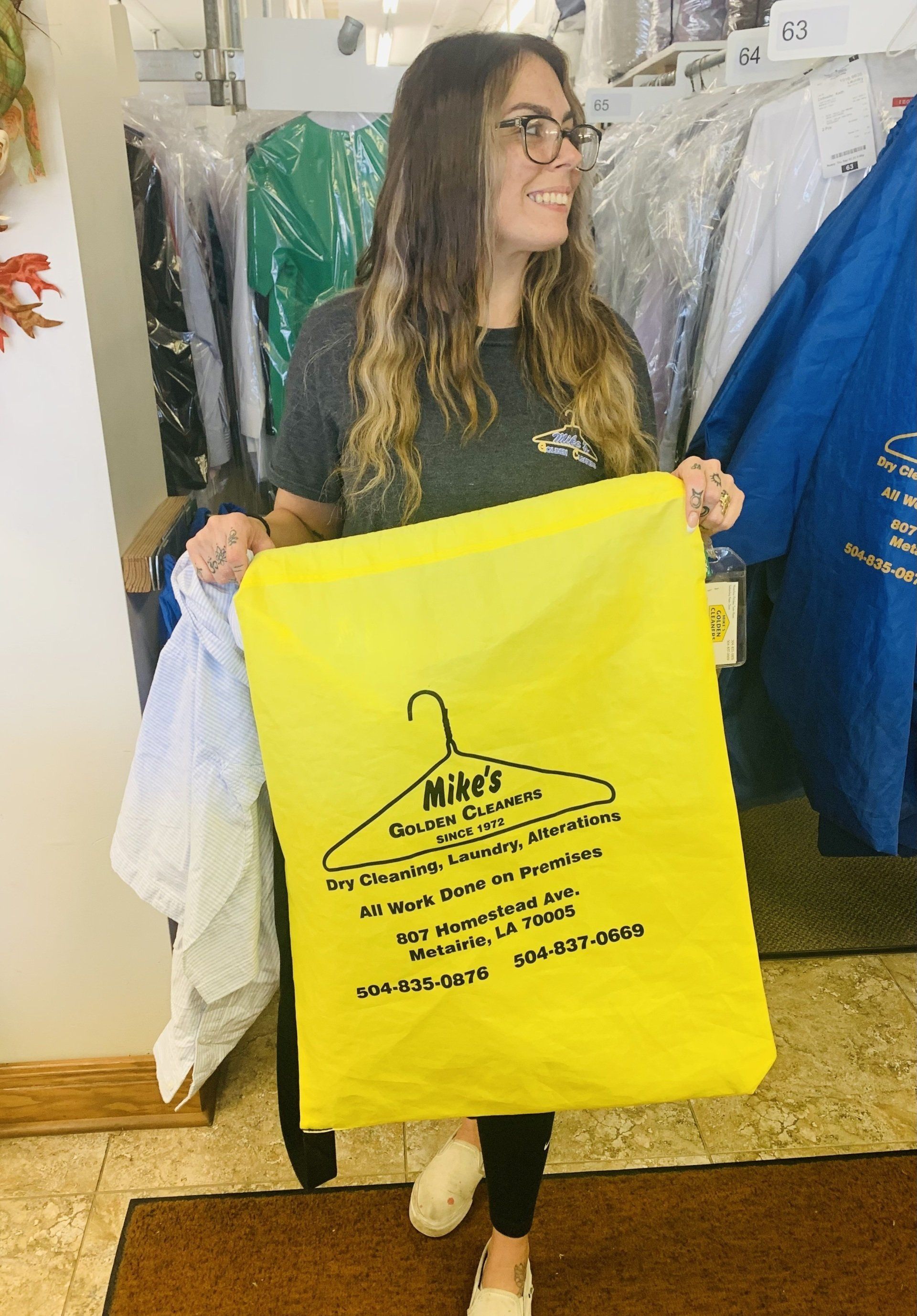 Woman holding a bright yellow garment bag in a clothing store, with racks of clothes behind her.