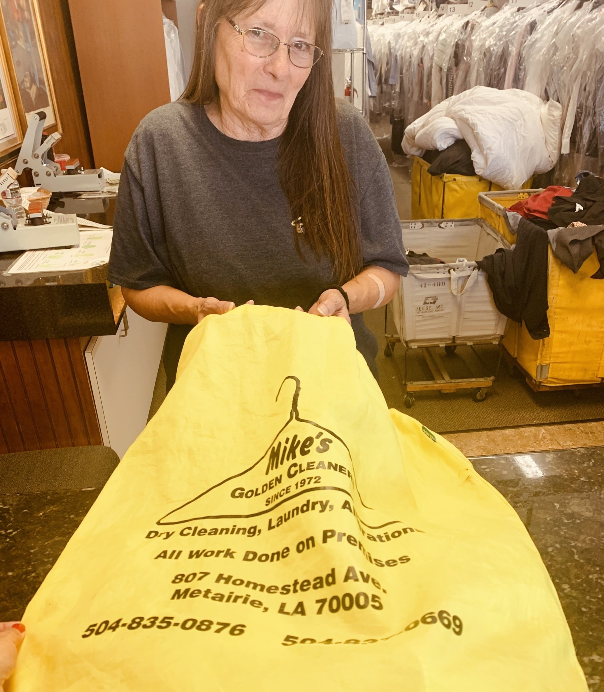 Woman holding a large yellow garment bag in a clothing shop.