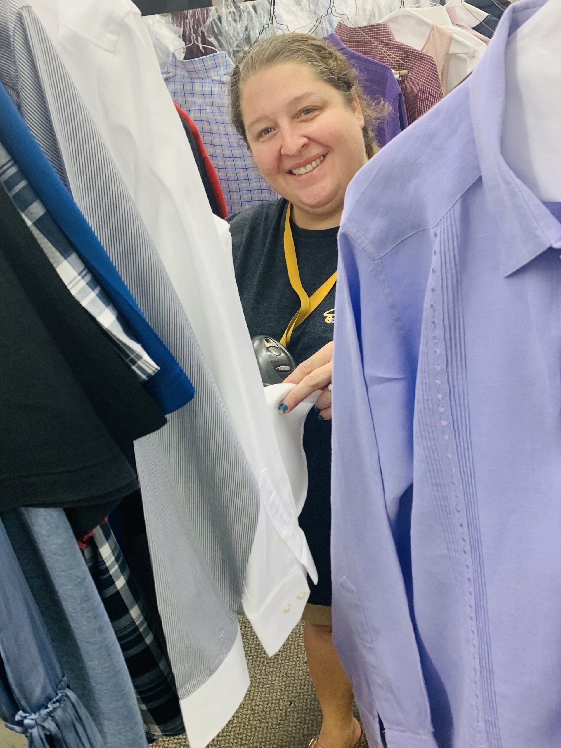 Smiling person peeks between hanging clothes in a thrift store aisle