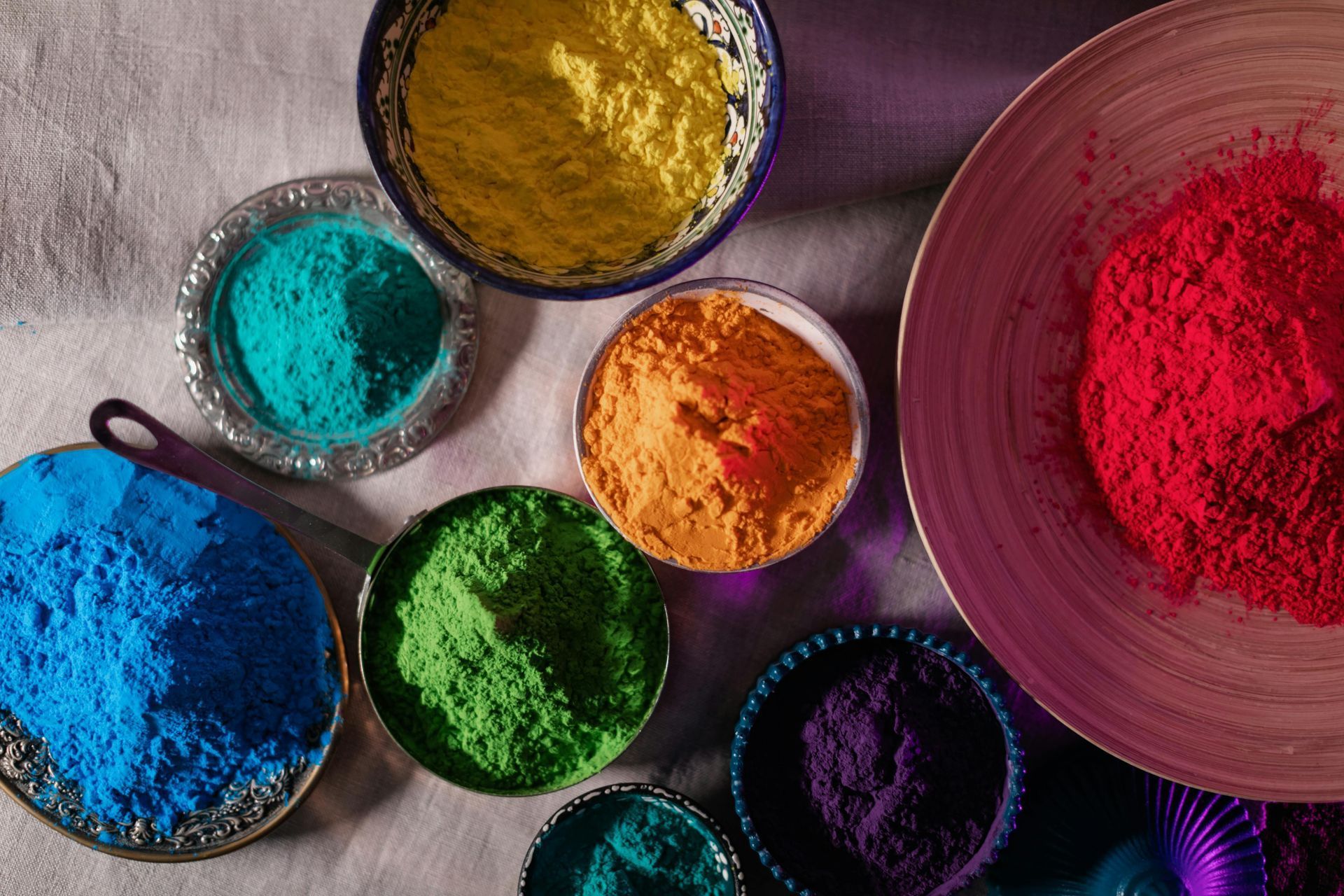 Assorted bright powders in bowls and piles on a textured cloth background.