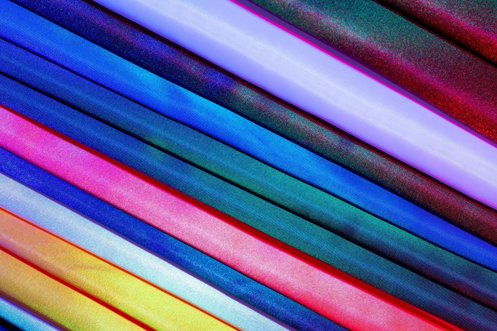 Colorful diagonal rolls of textured fabric or ribbon in blue, purple, pink, yellow, and red.