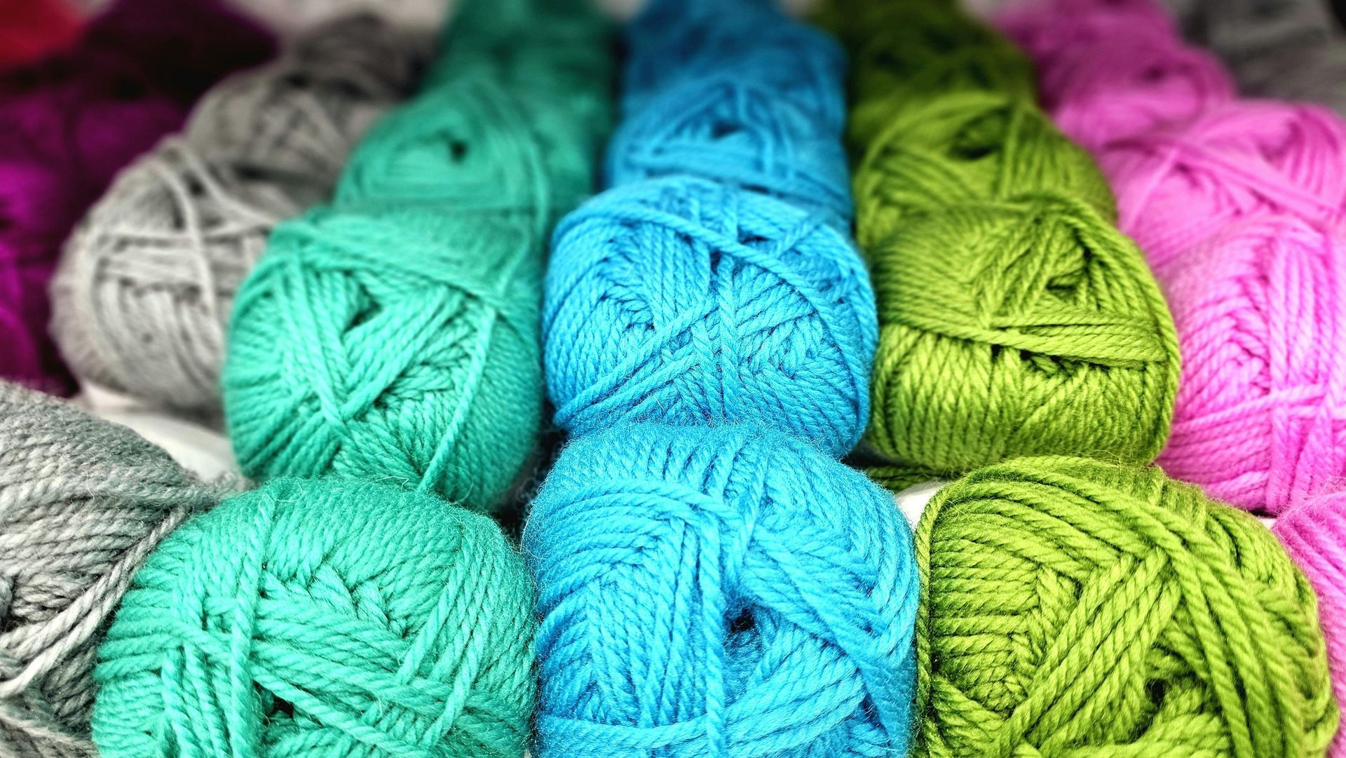 Colorful skeins of yarn in white, gray, turquoise, blue, green, and pink arranged in a close-up pile