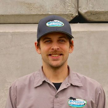 Smiling man in a dark cap and gray work shirt standing against concrete blocks