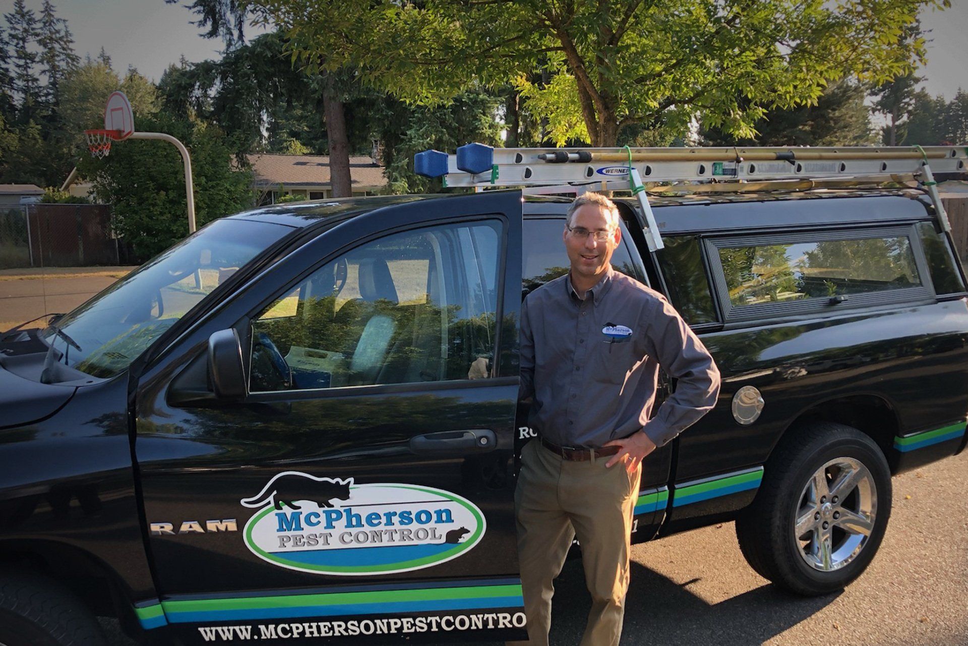 Man standing beside a black McPherson Pest Control truck in a sunny parking lot