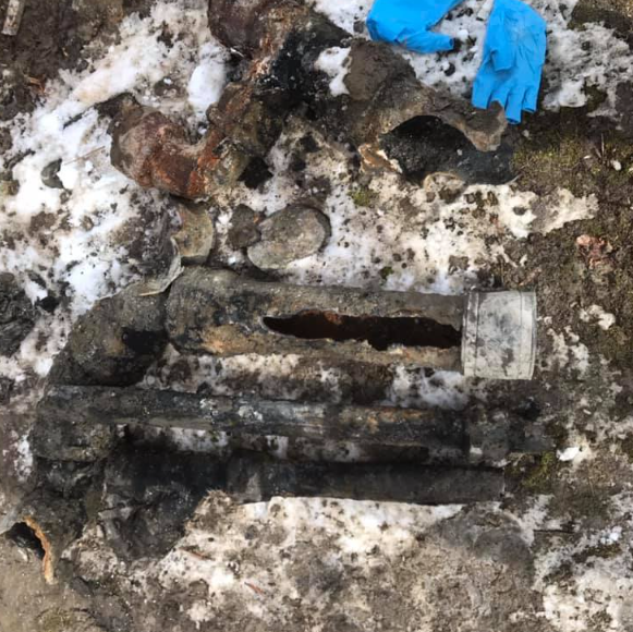 Mud and snow-covered ground with a rusted metal rod and blue gloves nearby