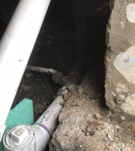 Damaged underground pipes and rubble in a narrow trench beside a wall