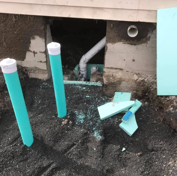 Open basement wall with two turquoise PVC pipes and scattered broken pipe pieces on dirt