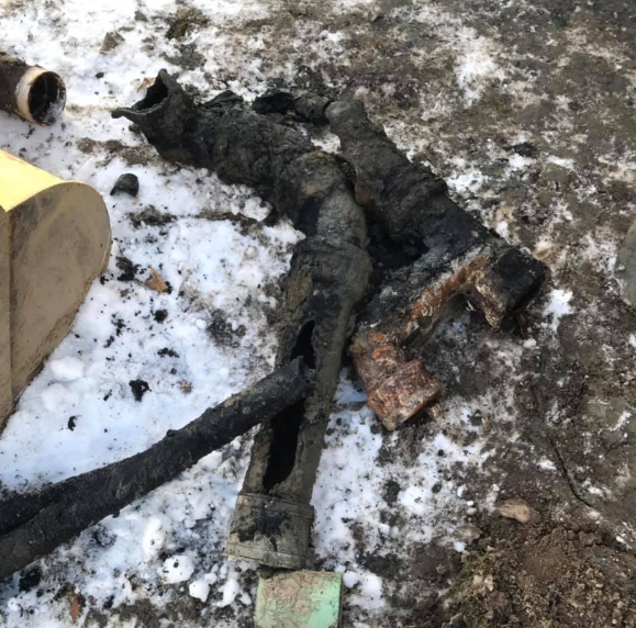 Burned black hose or cable lying on snowy ground near a charred pipe end