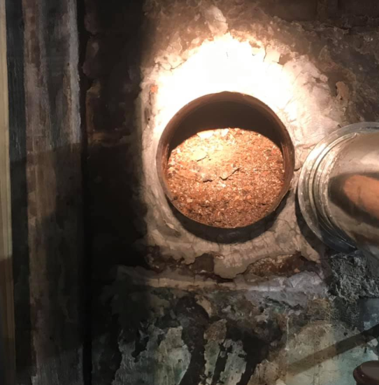 Rusty circular pipe opening in a dim, worn concrete wall with debris inside