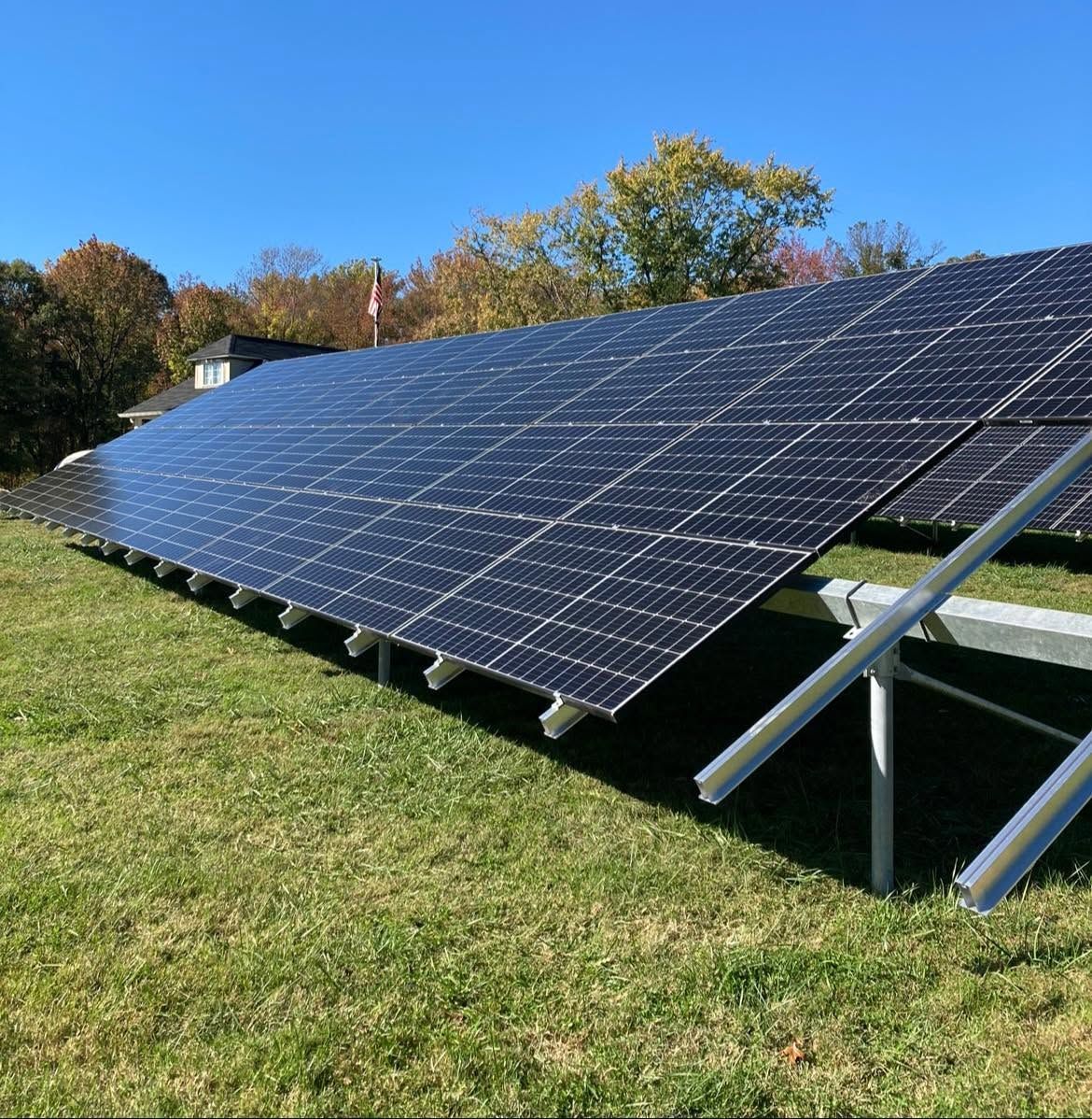 Large ground-mounted solar panel array in a grassy field under a clear blue sky