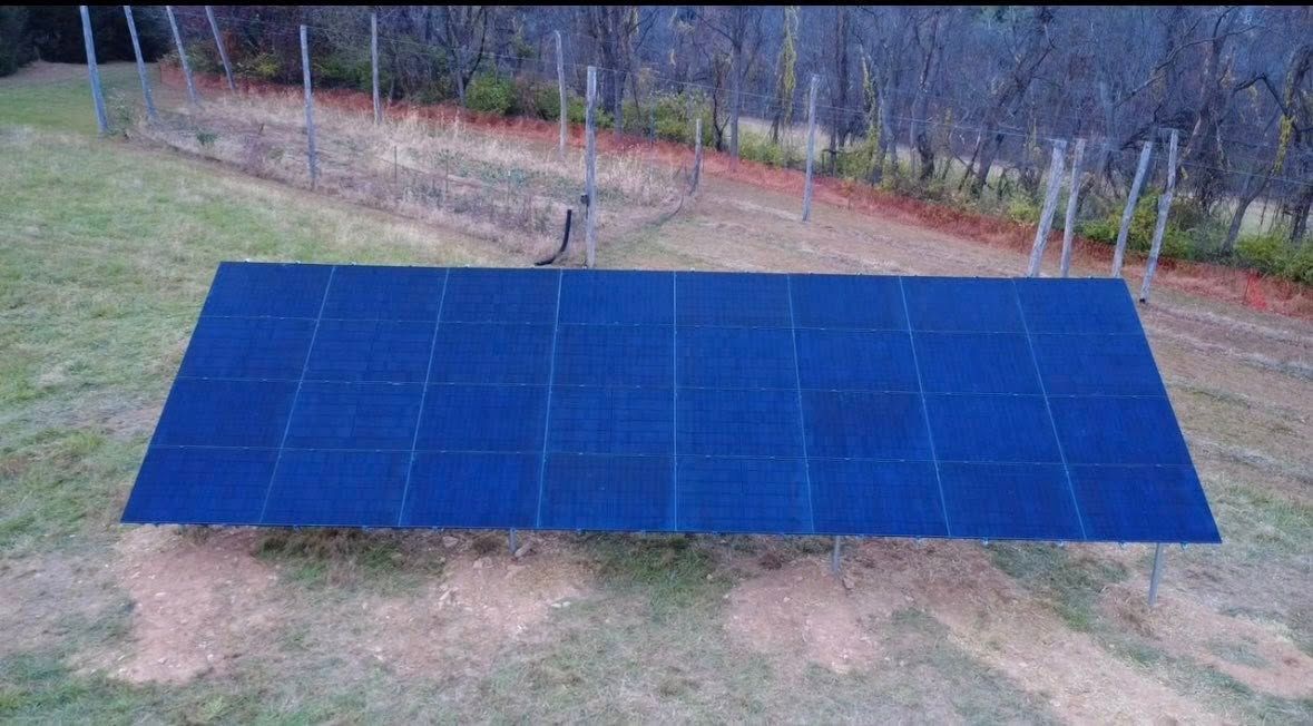 Large blue solar panel array on a grassy field with trees in the background.