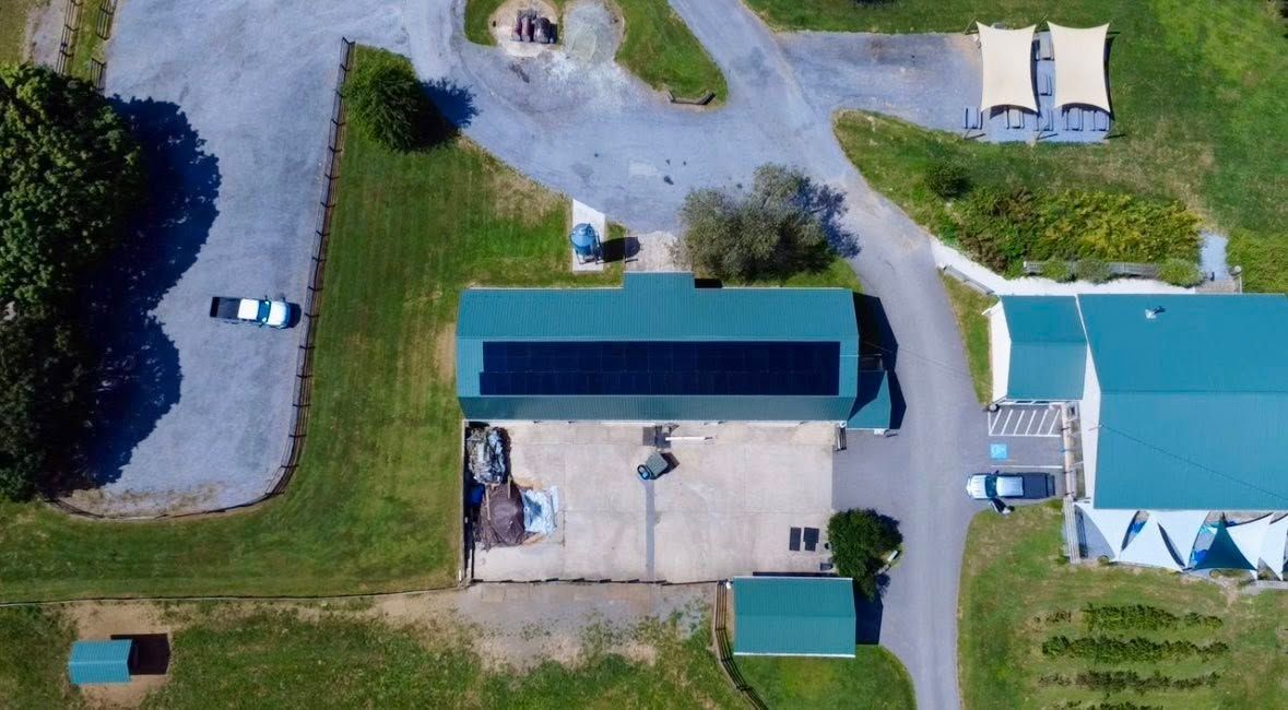 Aerial view of a small building, parking area, and turquoise swimming pool beside a grassy lawn.