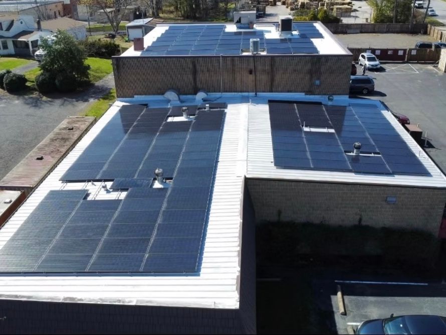 Aerial view of a flat roof covered in solar panels on a building in a parking lot.