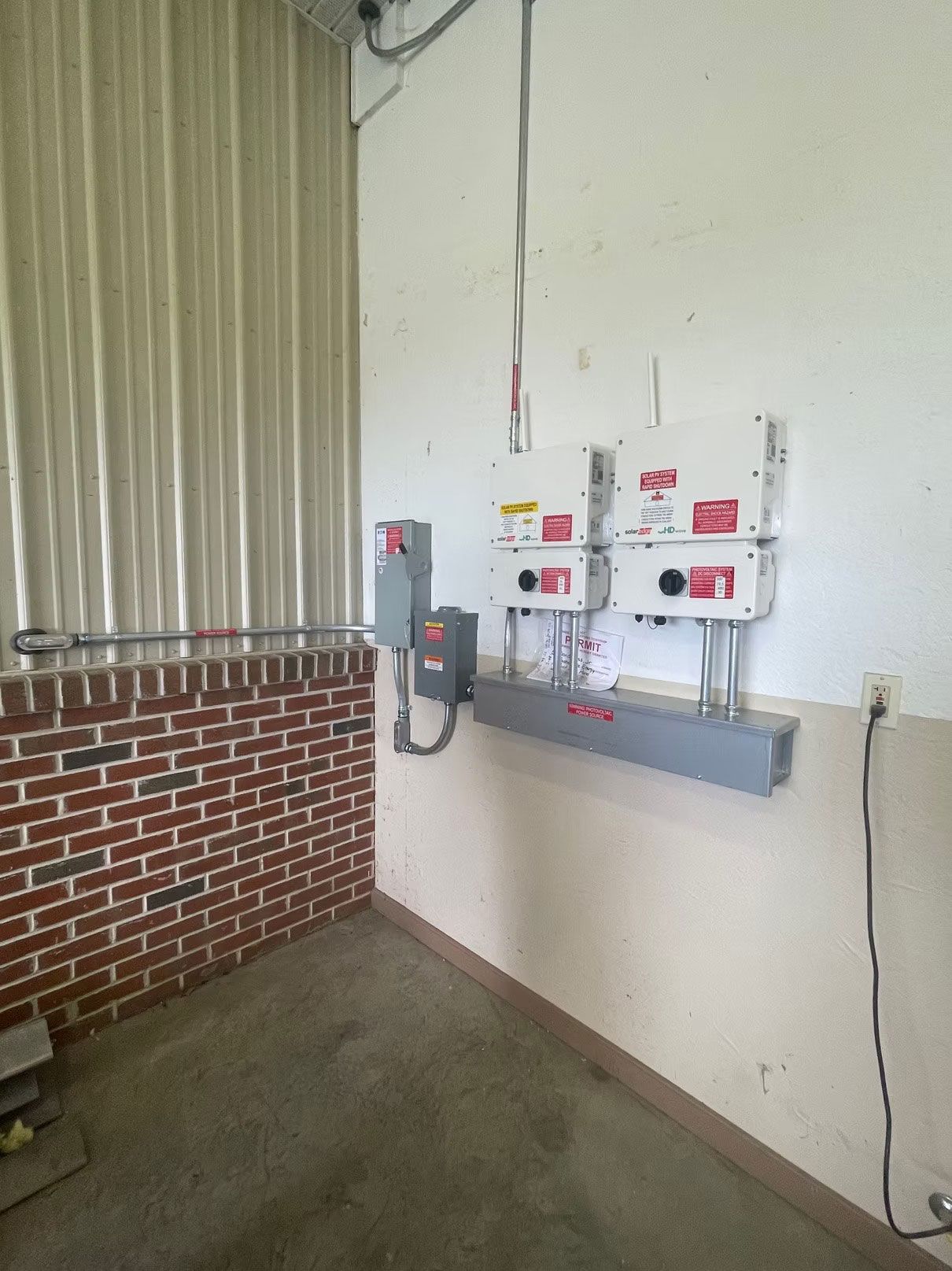 Wall-mounted emergency devices and panels on a white wall beside a brick interior
