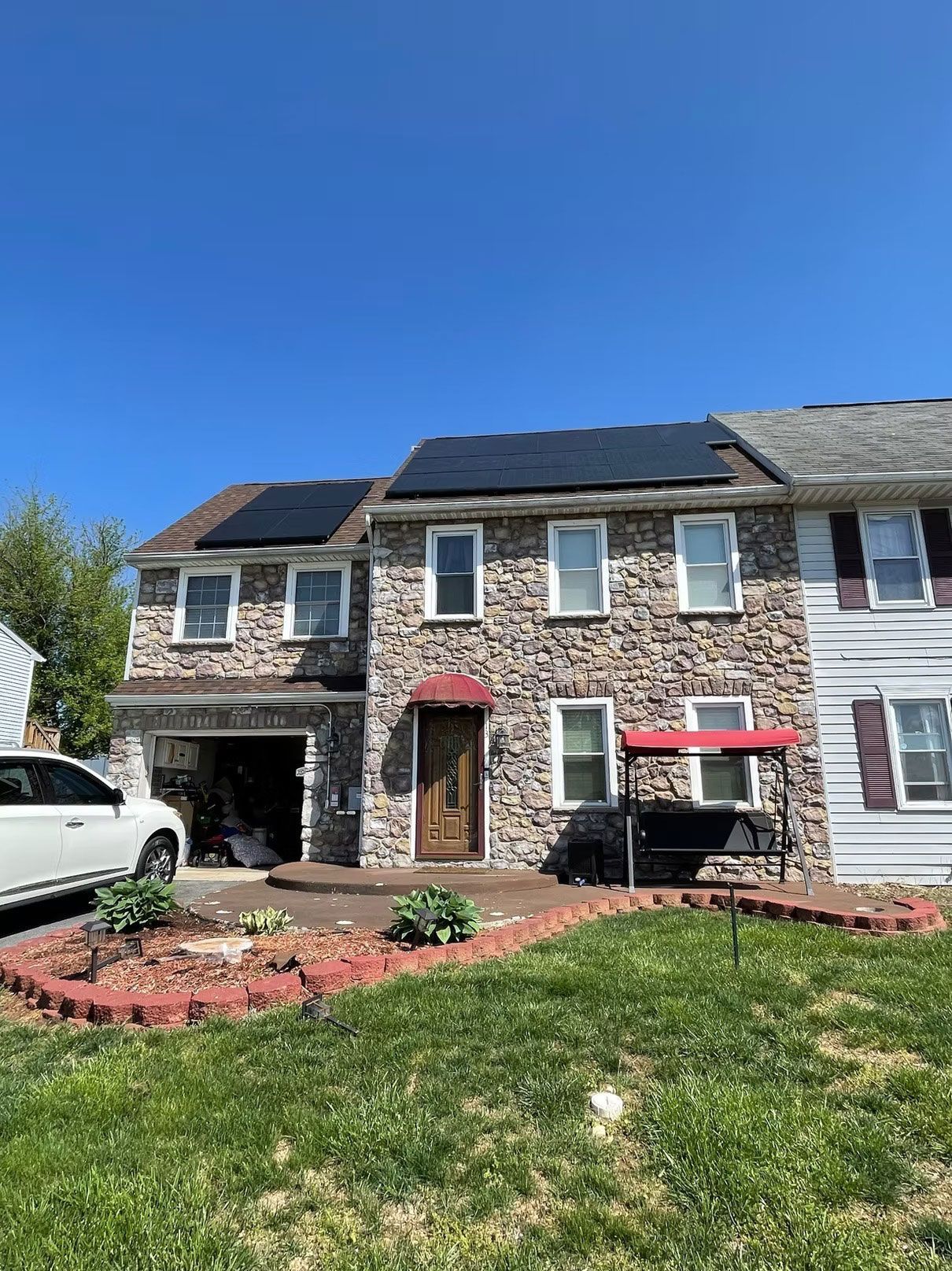 Two-story stone townhouse with a red awning, small garden, and parked car under a blue sky
