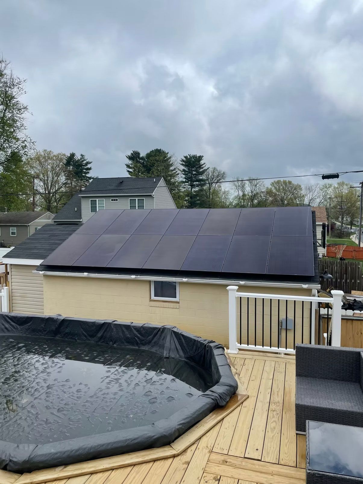 Backyard with solar panels on a shed, above an above-ground pool and wooden deck under cloudy skies