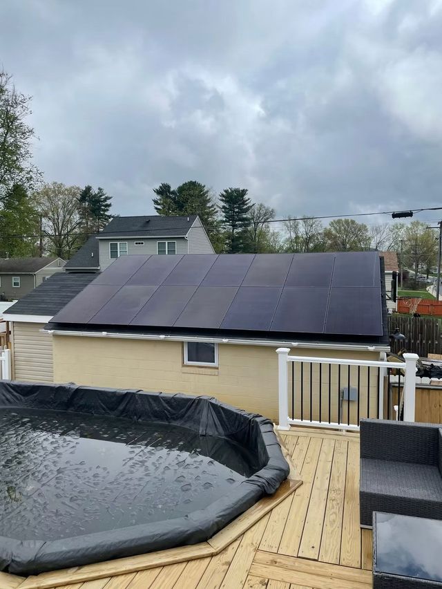 Backyard with a solar-panel roof, black-covered pool, and wooden deck under cloudy skies