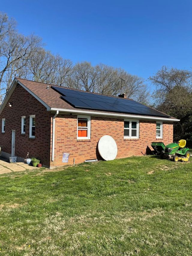 Brick house with solar panels on the roof, white satellite dish, and a grassy yard under a blue sky.