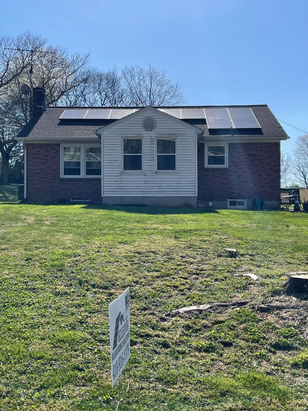 Small brick house with solar panels on the roof and a grassy yard in front