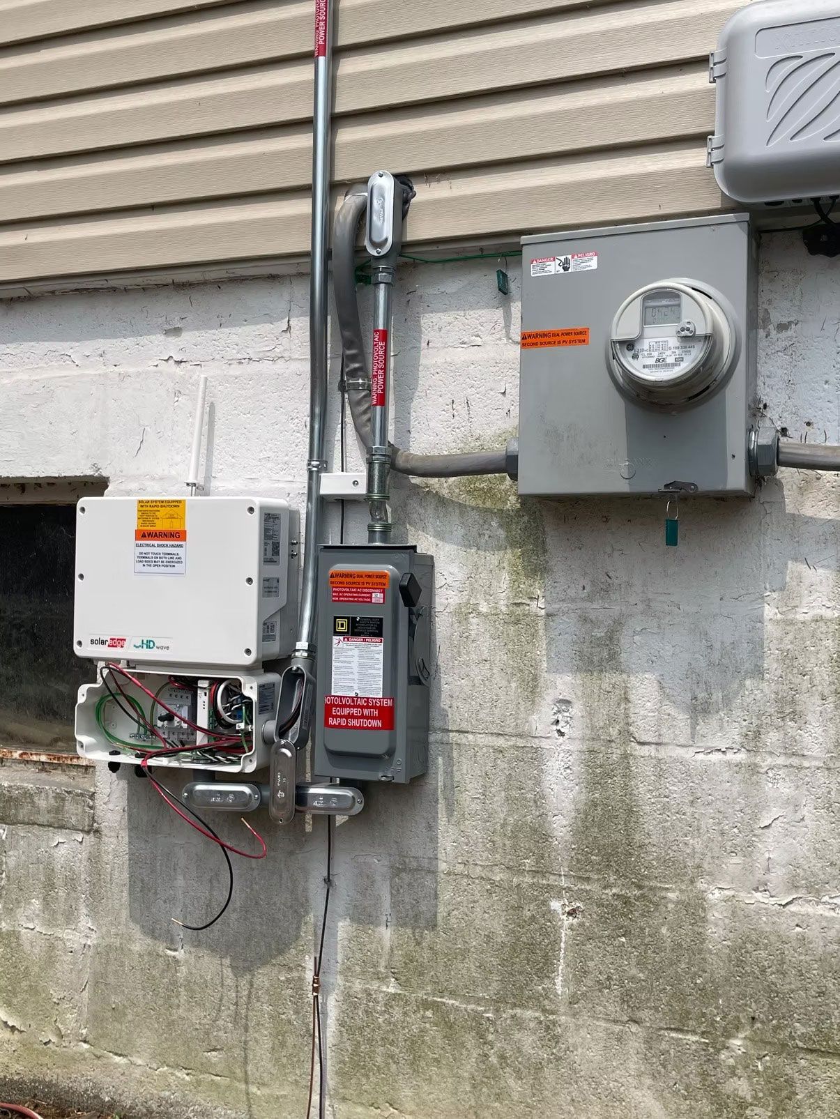 Outdoor electrical meter and utility boxes mounted on a concrete wall beside a building.