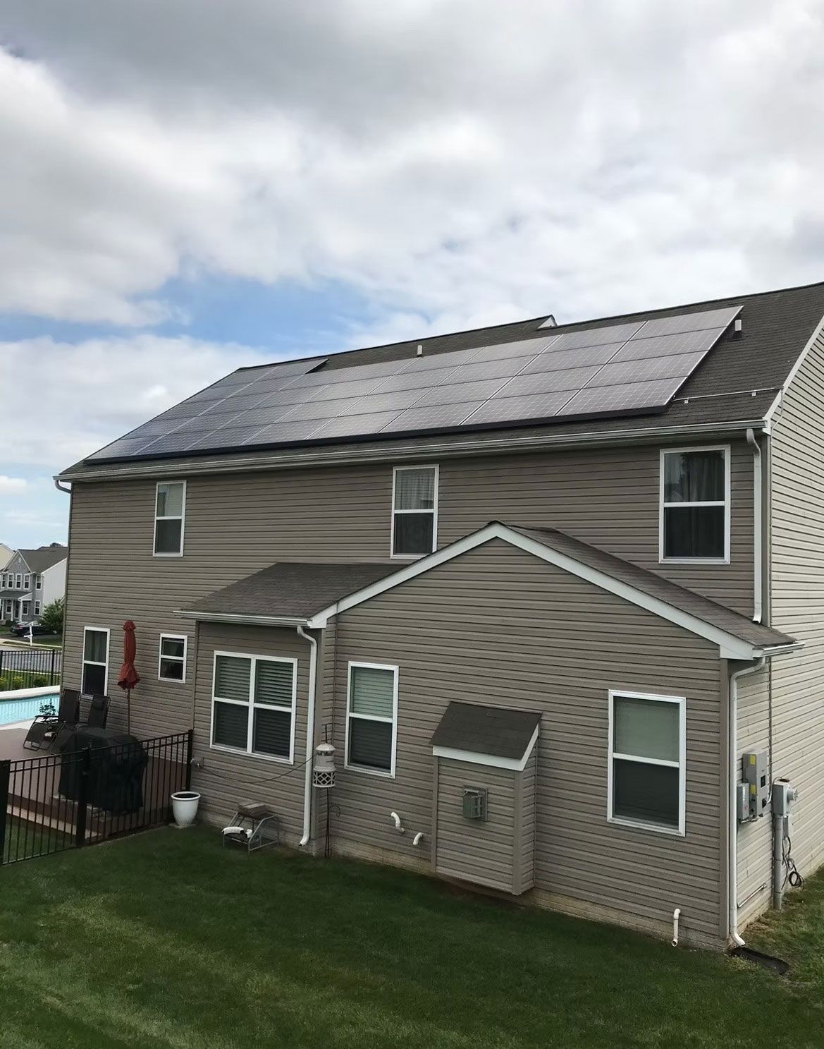 Two-story beige house with solar panels on the roof and a green lawn in front