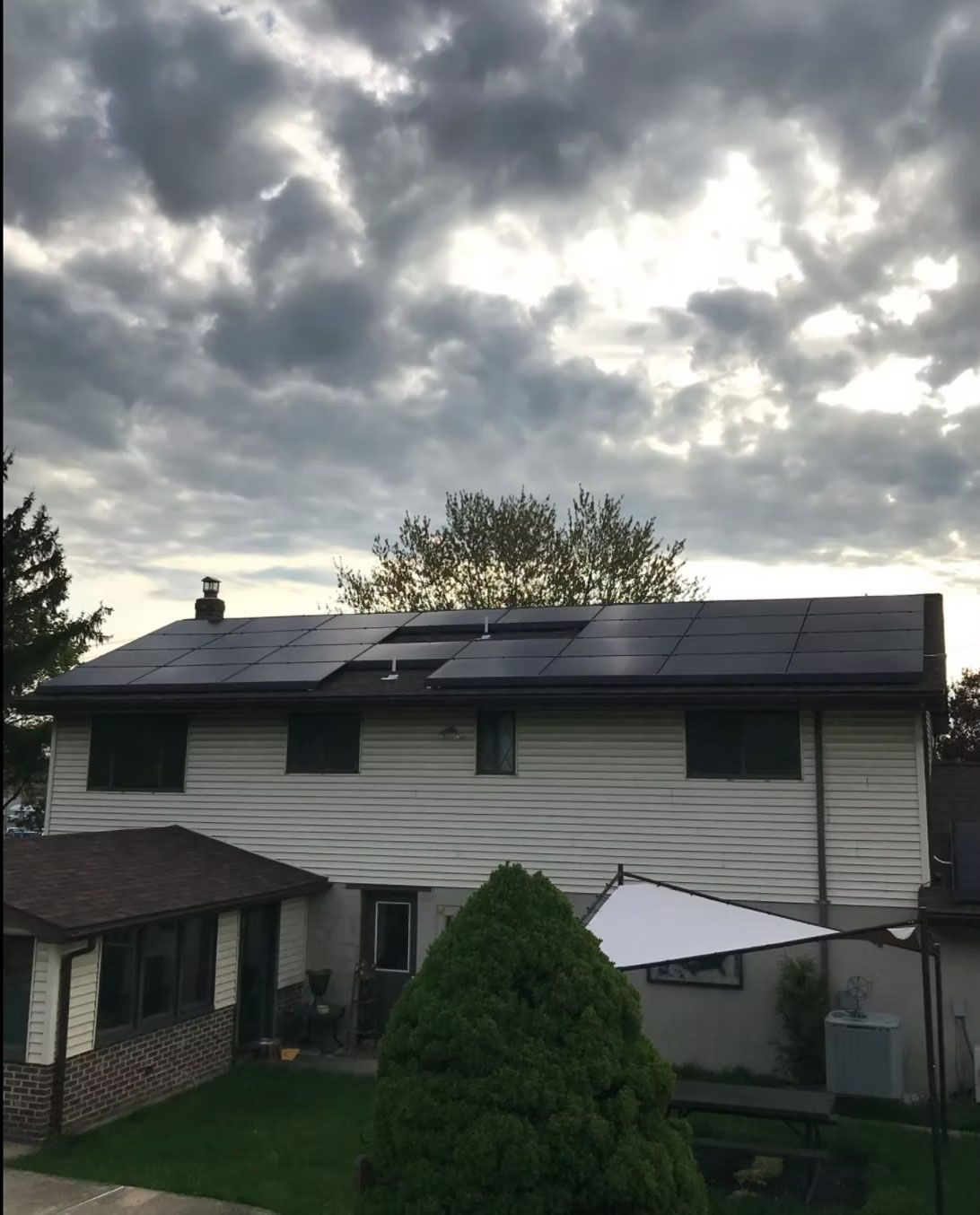 Suburban house with solar panels under a cloudy sky, viewed from the yard.