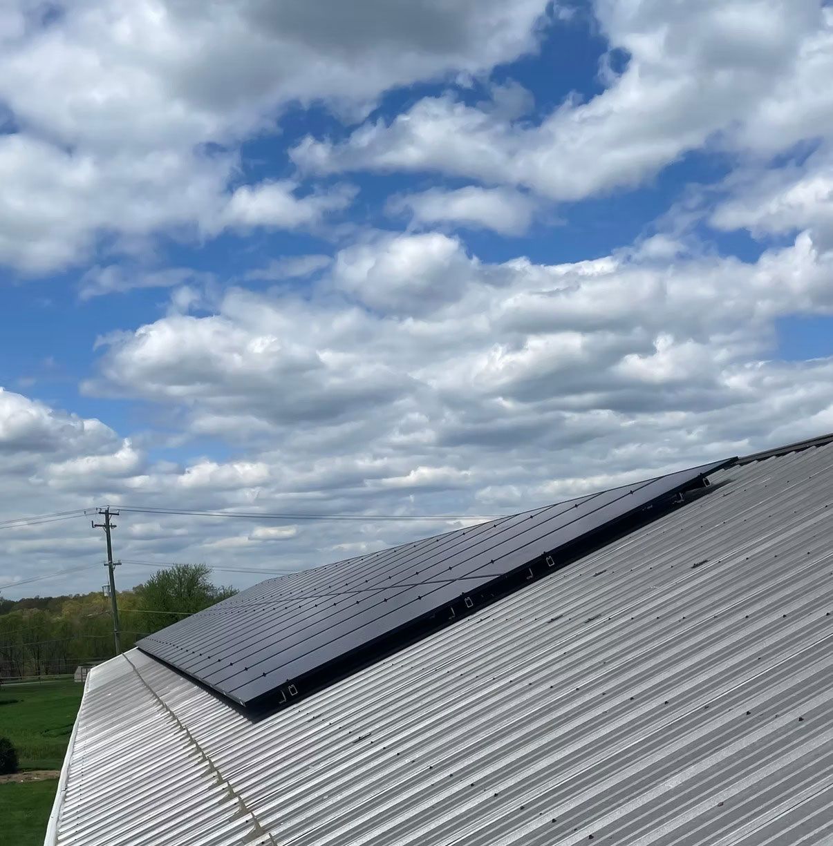 Solar panels on a corrugated metal roof under a cloudy blue sky.