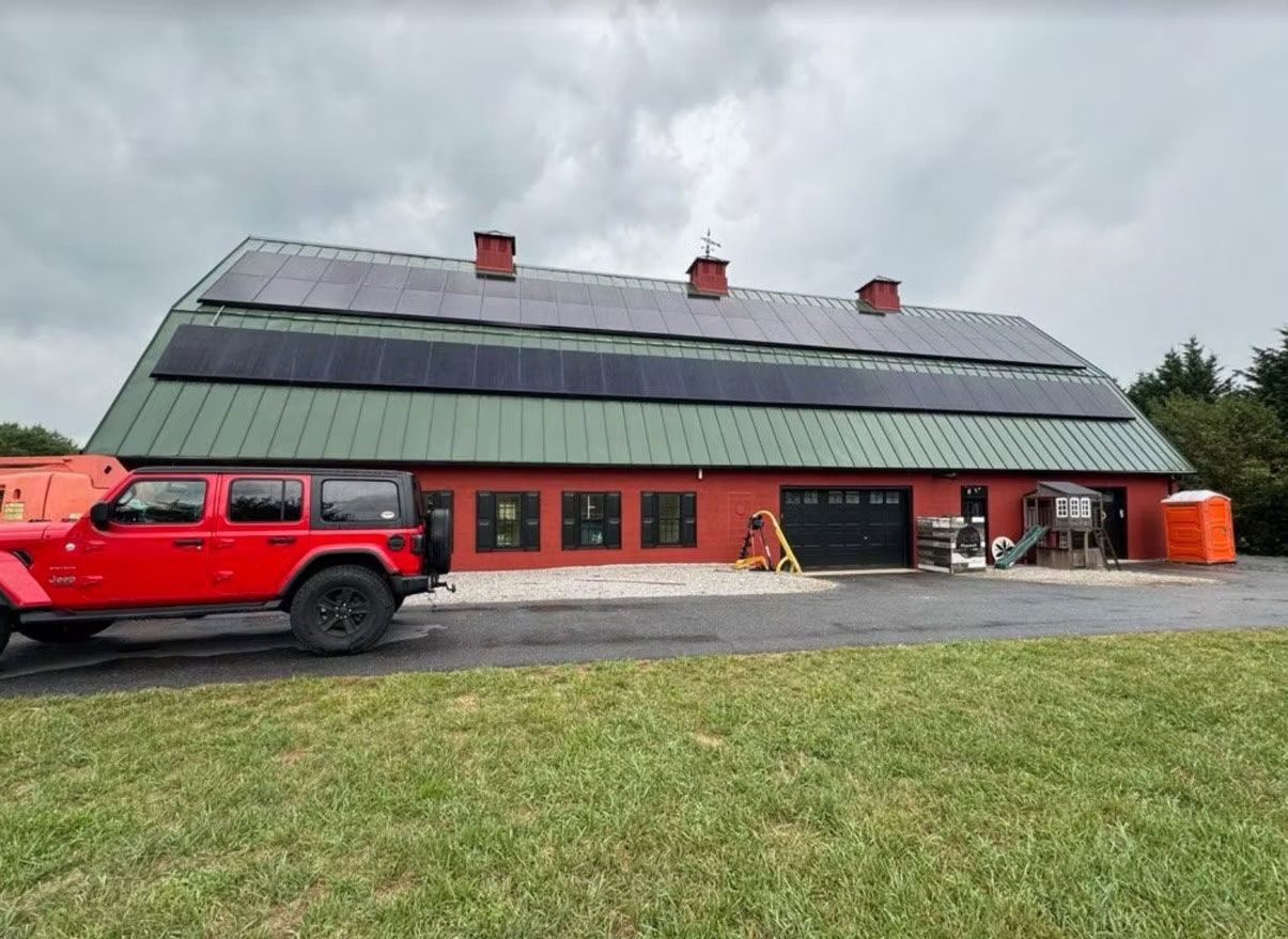 Red vehicle parked beside a long building with a sloped dark roof and solar panels under cloudy sky
