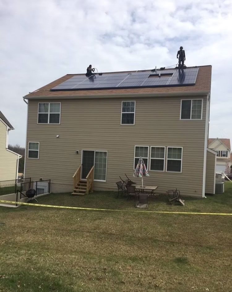 Workers on a roof installing solar panels on a beige two-story house.
