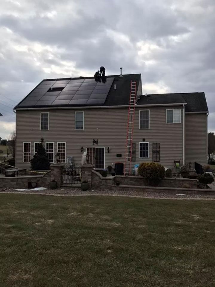 House with solar panels on the roof and a person working near the top under a cloudy sky