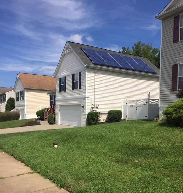 Suburban house with solar panels on the roof, viewed from a sloped lawn beside a sidewalk.