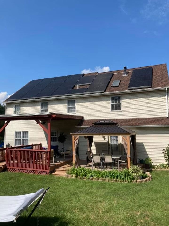 Suburban house with solar panels, patio seating, and a green backyard under a blue sky
