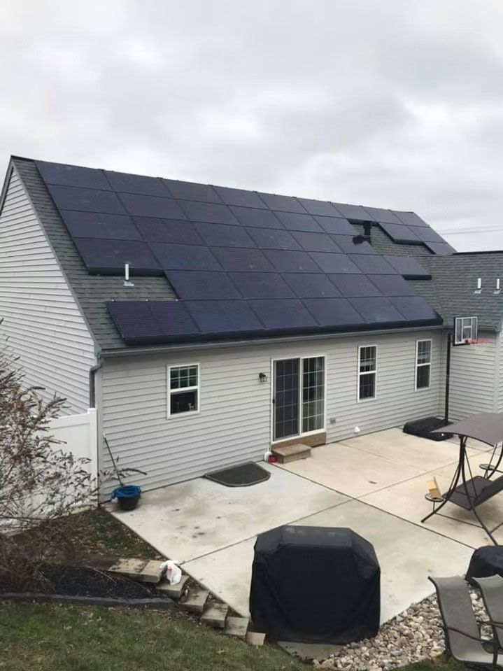 House with a large black solar panel roof and a concrete patio in front