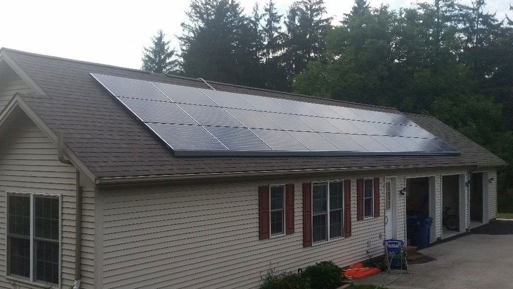 Single-story house with a large rooftop solar panel array and white siding.