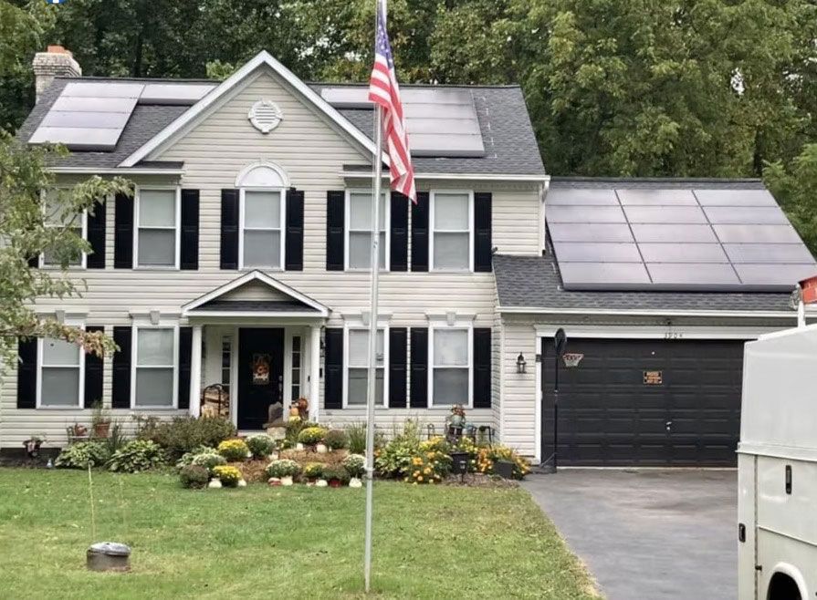 Two-story gray house with solar panels, black shutters, and an American flag in front yard.