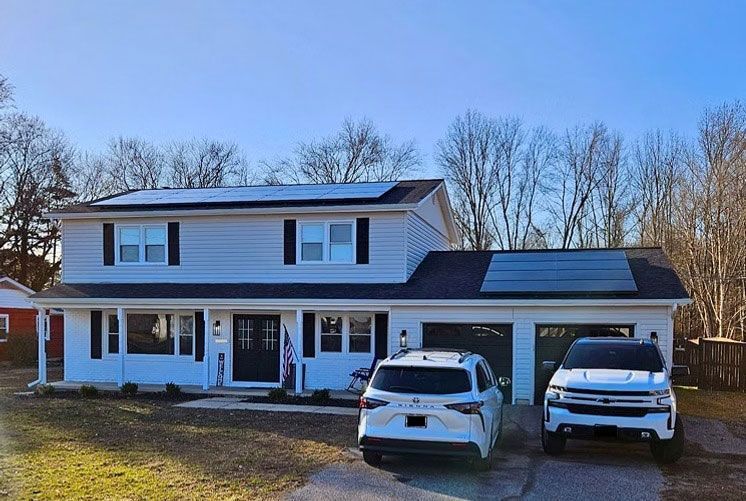 Two-story white house with dark roof and two white SUVs parked in the driveway.
