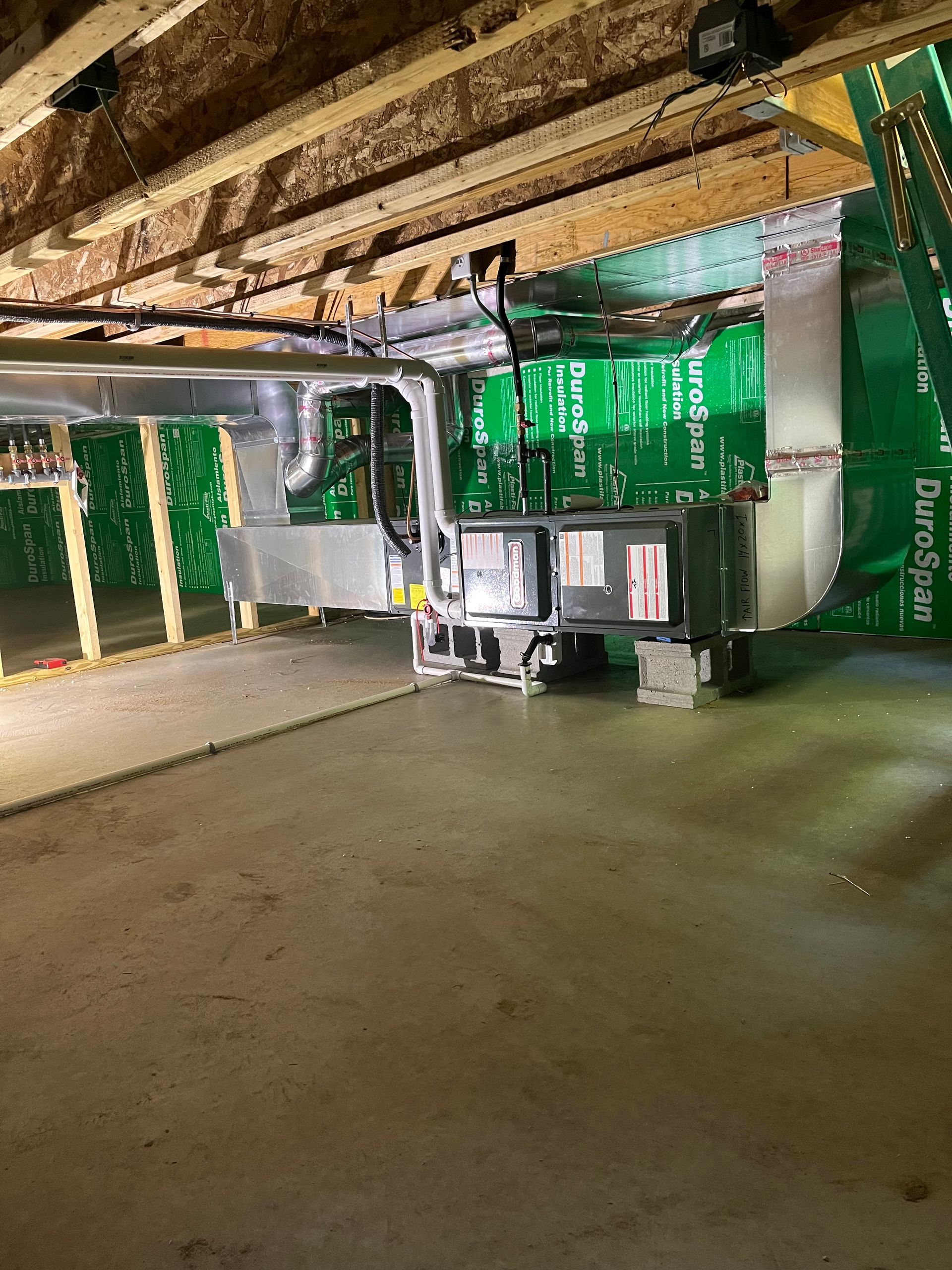 HVAC unit installed in a basement, featuring metal ductwork connected to a furnace, set against a green vapor barrier.
