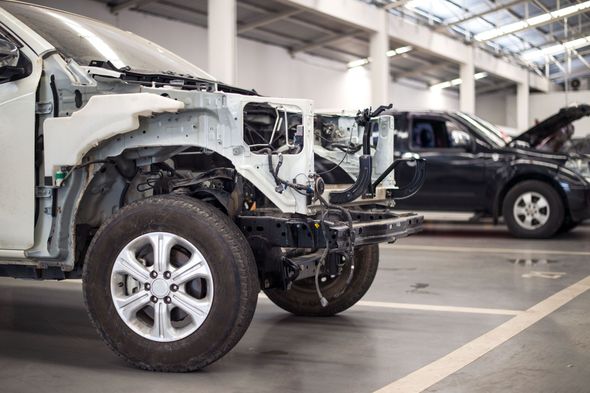 White truck undergoing repair in a repair shop; front end dismantled, other vehicles in background.