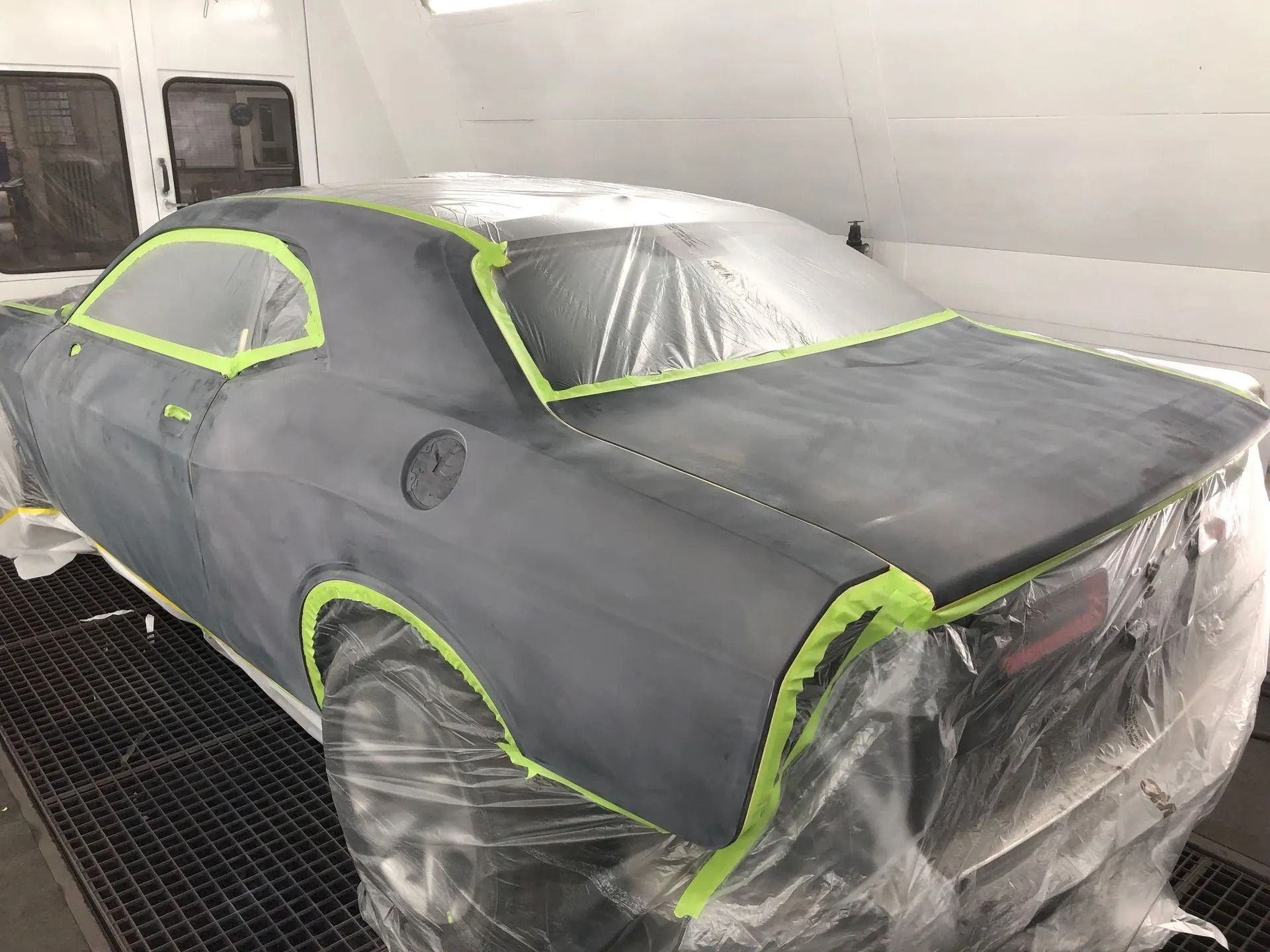 Dark gray car in a paint booth, taped and covered in plastic, ready for paint.