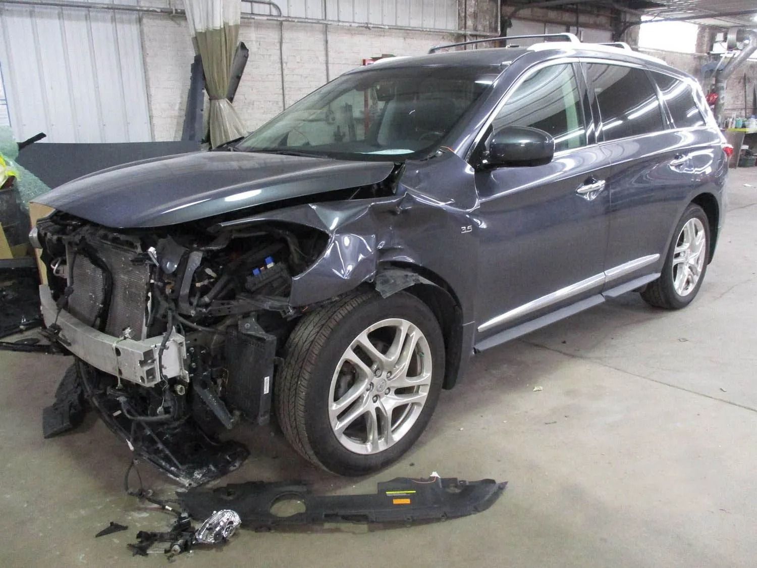 Damaged gray SUV in a repair shop, front end heavily damaged.