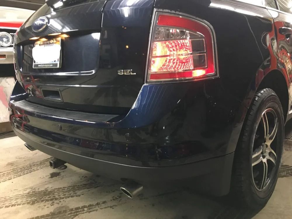 Dark blue Ford Edge SUV rear view, with taillight illuminated, parked indoors.