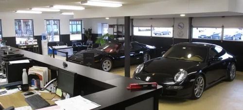 Interior of a car dealership with several black cars, including a Porsche, in the showroom.