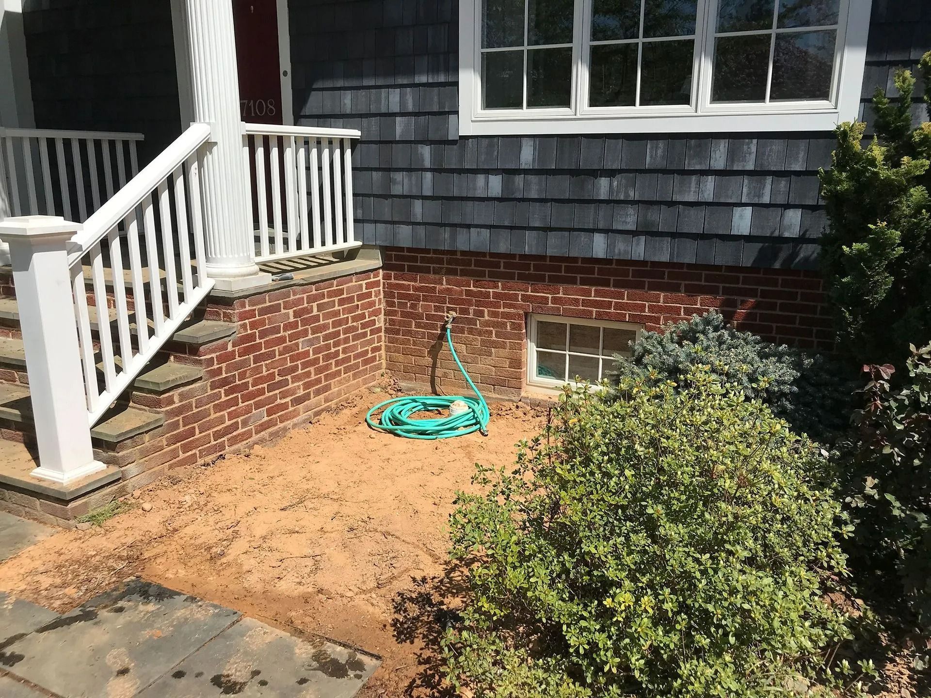 Brick house entrance with a white porch railing, steps, and a garden hose on the ground.
