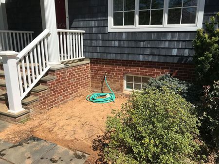 Brick house entrance with a white porch railing, steps, and a garden hose on the ground.