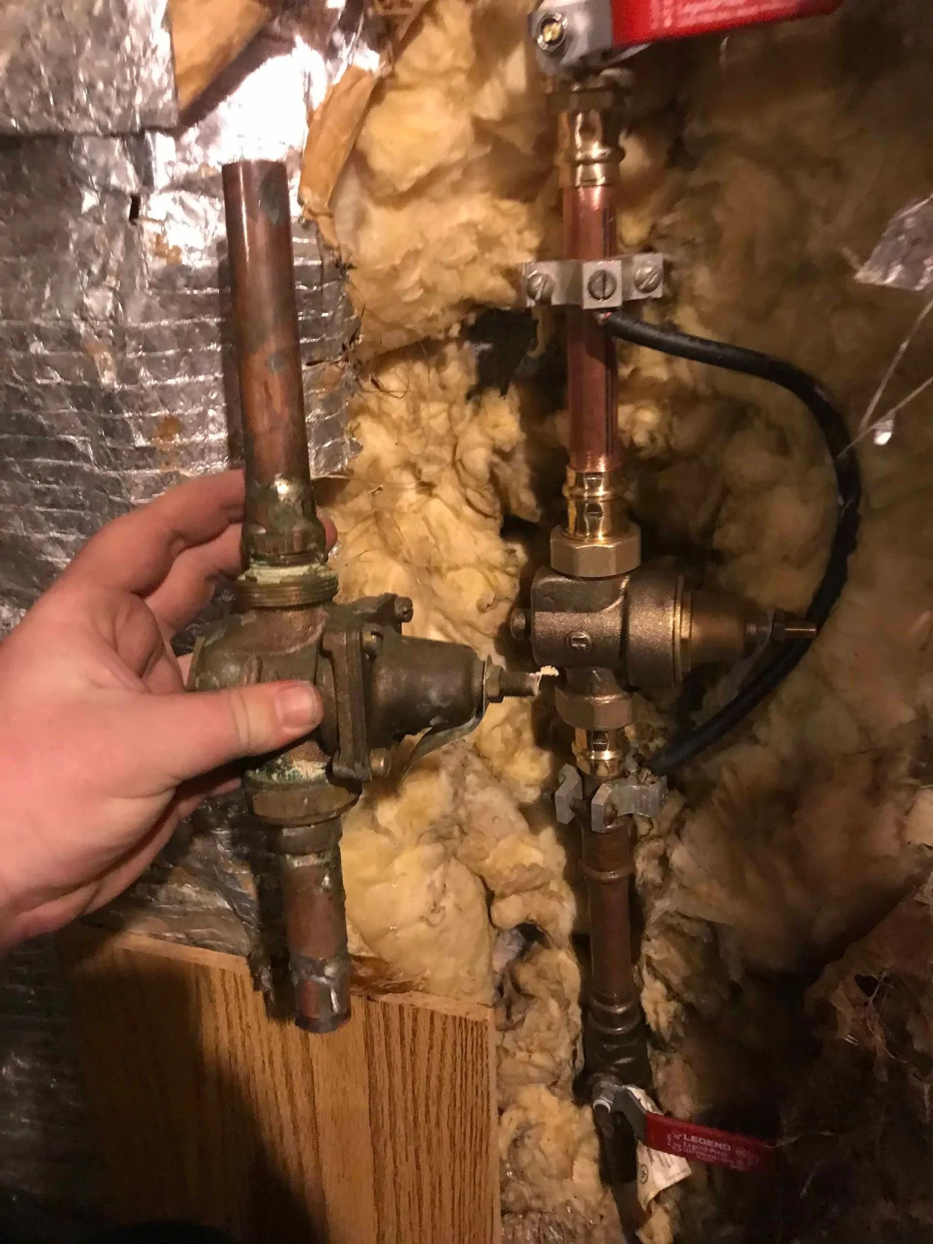 Hand holding a pipe connected to plumbing, with insulation visible behind it.