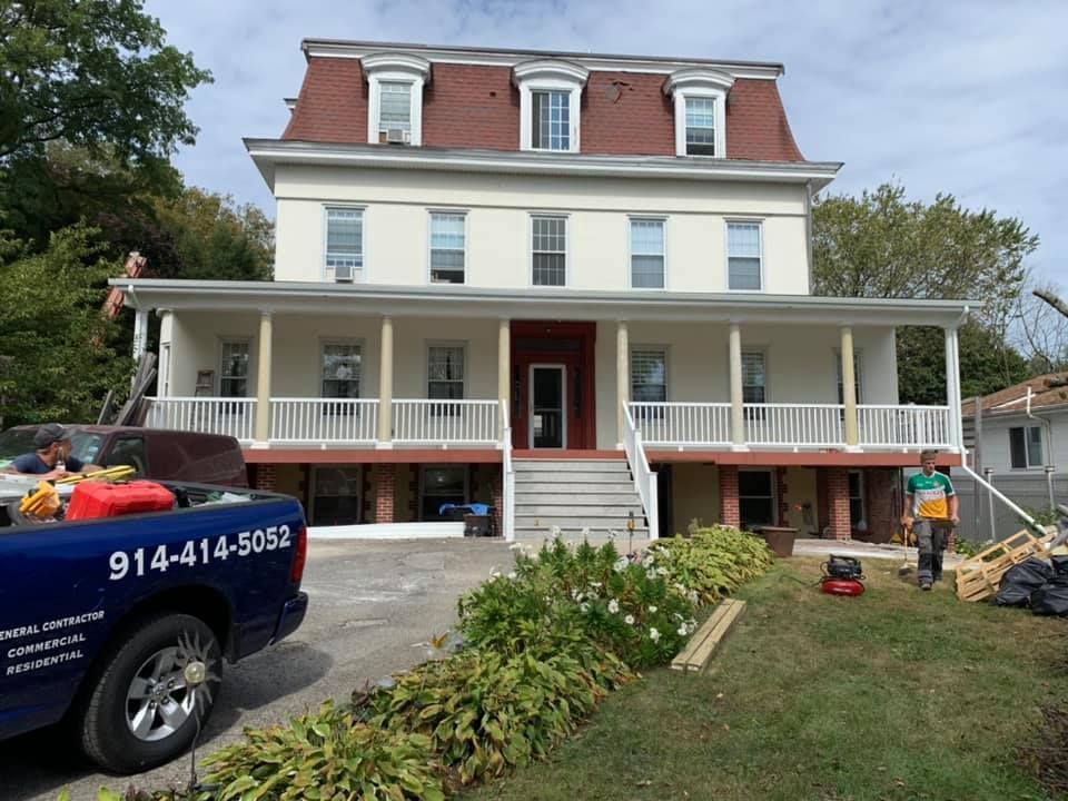 A blue truck is parked in front of a large white house