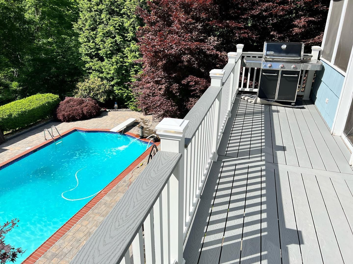 A deck with a grill and a pool in the background